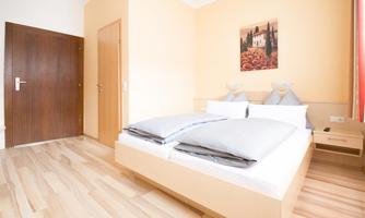 A cozy bedroom with a large double bed and wooden floor. A colorful picture hangs on the wall, and the atmosphere is bright and inviting.