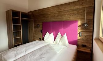 A modern bedroom with wooden walls and a comfortable double bed. The colored accents and the large ceiling lamp create an inviting atmosphere.