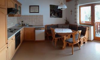 A modern kitchen with wooden cabinets and a dining area. Large windows provide plenty of daylight and a view outside.
