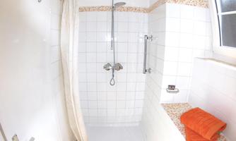 A modern shower with white tiles and an orange towel. Bright light shines through a window.