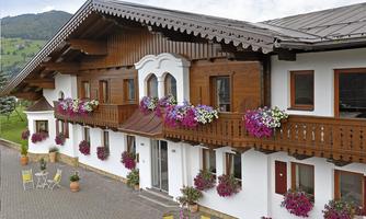 A traditional Alpine house with wooden cladding and colorful flower boxes. The cozy atmosphere is enhanced by the surrounding green landscape.
