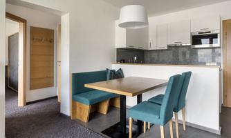 A modern kitchen with a dining table and seating areas in soft colors. The room feels bright and inviting.