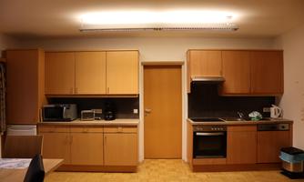 A modern kitchen with wooden cabinets and a bright light source. It features basic appliances such as a stove, a refrigerator, and a microwave.