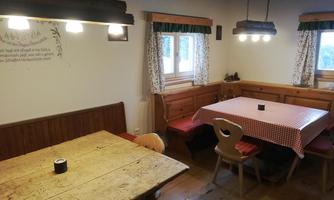 A cozy dining area with wooden chairs and tables. The walls are light and the windows provide plenty of daylight.