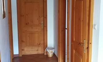 A bright hall with wooden ceilings and brown tiles. Several wooden doors lead to different rooms.