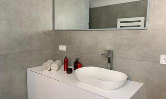 A modern bathroom with gray walls and a white sink. On the vanity, there are towels and some red decorative bottles.