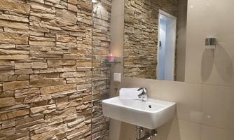 A modern bathroom with a natural stone wall and an elegant sink. The mirror and soft lighting create a pleasant atmosphere.