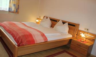 A cozy bedroom with a large double bed and wooden details. Next to the bed is a bedside table with a lamp.