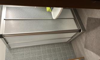 A modern bathroom with a shower cabin and a sink. There are towels on a shelf and a gray rug on the floor.