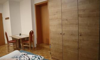 A simple room with a wooden wardrobe and a table with two chairs. The walls are light and the floor is made of wood.