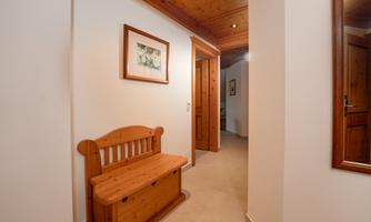 A bright hallway with a wooden bench and a wall painting. The walls are white and the ceiling has wooden beams.