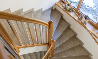 An elegant spiral staircase with a wooden railing and modern tiles. The view leads down to a window that lets in light.