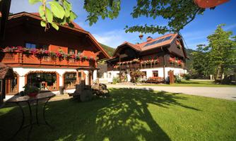 A cozy country house with blooming balcony flowers and a green garden. The sun is shining and the sky is blue.