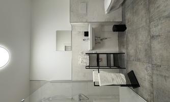 A modern bathroom with a walk-in shower and a sink. There is a towel rack on the wall and the floor is made of gray tiles.