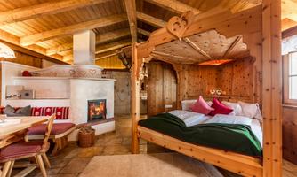 A cozy bedroom with a wooden four-poster bed and an open fireplace. The walls are clad in wood, creating a warm atmosphere.