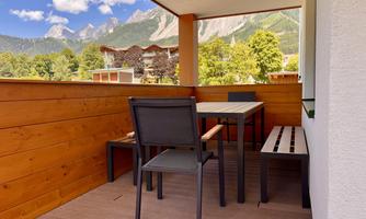 A cozy balcony with a table and chairs. In the background, mountains and a green landscape can be seen.