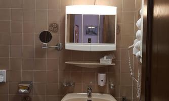 A small bathroom with a sink, a mirror, and a toilet. The walls are tiled in a warm brown color.