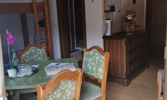 A cozy dining area with a table and chairs. In the background, a wardrobe and a window are visible.