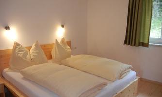 A cozy bedroom with a double bed and large pillows. The walls are light, and a window lets soft light in.