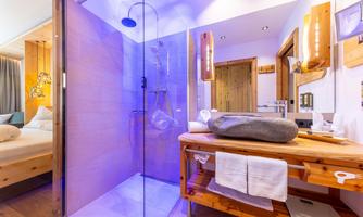 A modern bathroom with a glass shower cabin and wooden shelves. The soft lighting creates a relaxed atmosphere.