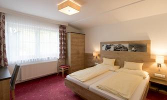 A comfortable room with two single beds, a desk, and a window with curtains. The walls are light and the decor is modern and inviting.