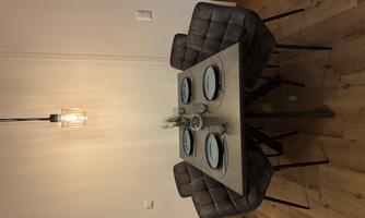 A modern dining area with a square table and four gray chairs. The table is elegantly set with plates and a small plant in the center.