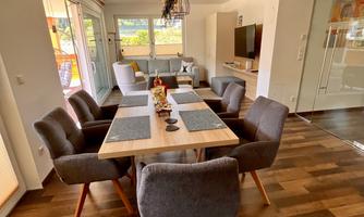 A modern dining room with a large table and comfortable chairs.  
  
Large windows let in plenty of daylight and offer a view outside.