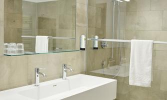 A modern bathroom with a large sink and a mirror. The walls are covered with light tiles, and there are towels and toiletries.