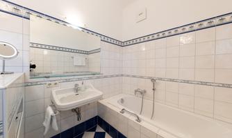 A bathroom with a bathtub and a sink. The walls are decorated with white tiles and blue accents.