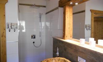 A modern bathroom with a shower and an elegant wooden sink. The walls are light tiled and the lighting creates a pleasant atmosphere.