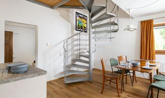 A modern interior design with a curved staircase. The room is brightly lit and equipped with wooden details as well as a dining table.
