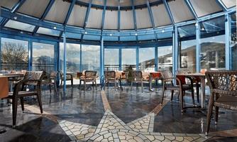 A modern restaurant with large windows and a beautiful view. The floor is designed with an eye-catching mosaic pattern, and there are comfortable chairs available.