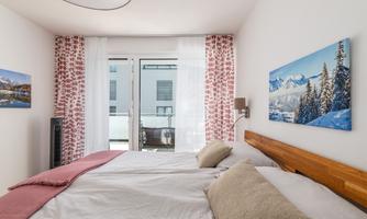 A cozy bedroom with two beds and a wooden frame. Large windows let in plenty of light and provide a view of the outdoor terrace.