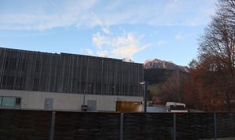 A modern building with wooden cladding and metallic elements. In the background, there are snow-covered mountains and a blue sky.
