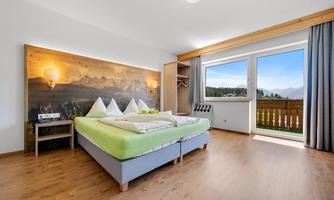 A modern bedroom with a double bed and wooden flooring. The room has a window with a view of the mountains and is bright and inviting.