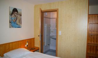 A simple room with a bed and a nightstand. In the background, there is a bathroom and a picture on the wall.