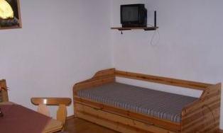 A simple room with a wooden bed and a television on the wall. A wooden table and chairs can also be seen.
