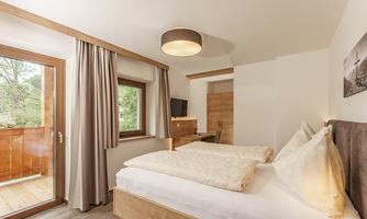A bright, modern bedroom with a double bed and cozy pillows. There are large windows that offer a beautiful view outside.