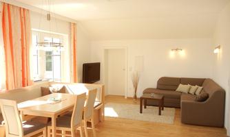 A bright living room with a cozy sofa and a dining area. Large windows let in plenty of light and give the room a friendly atmosphere.