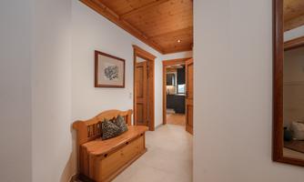 A cozy hallway with a wooden bench and a cushion. The walls are painted light, and the ceiling has wooden paneling.