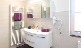 A modern bathroom with a sleek sink and large mirrors. Towels in various colors hang on a towel rack.