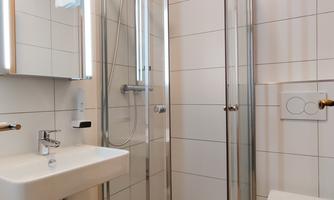 A modern bathroom with a glass shower, a sink, and a toilet. The walls are tiled with white tiles, and there is a large mirror.