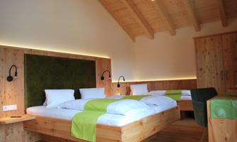 A cozy bedroom with two wooden beds and green blankets. The walls are bright, and the light creates a warm atmosphere.