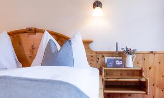 A cozy bedroom with a wooden bed frame and white bedding. Next to the bed is a nightstand with a small decoration.