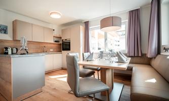 A modern kitchen with light wood and elegant furniture. The dining area is well-lit and inviting.