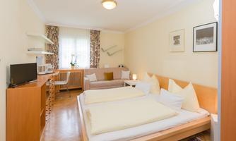 A bright and cozy room with two beds and a sofa bed. The walls are painted in soft colors, and a desk as well as a television are also available.