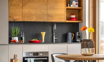A modern kitchen with wood and gray tones. There is a table with chairs and an adjoining window front that lets in a lot of light.
