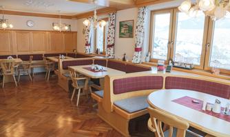 A cozy dining room with wood paneling and comfortable benches. Large windows offer a view of the surroundings.