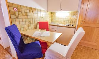 A small dining area with a table and three chairs in vibrant colors. The walls are tiled, and the kitchen is well-lit.
