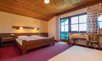 A cozy room with a wooden ceiling and red carpet. There are two beds, a table and chairs, as well as windows with curtains.